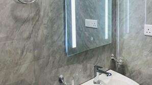 A bathroom with a marble floor, a glass-topped sink, a glass toilet paper holder, and a wall-mounted mirror with a light.