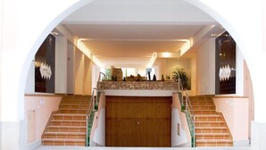 Una imponente escalera conduce a un techo alto, flanqueada por dos grandes ventanales con detalles decorativos.