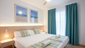 A hotel room with two beds, a ceiling fan, a nightstand, and a window with curtains.
