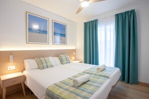 Una camera d'albergo con due letti, una ventola a soffitto, un comodino e una finestra con tende.