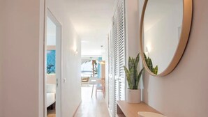 A hallway with a wooden bench, a round mirror, and a potted plant.