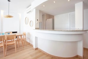 A modern kitchen with a curved countertop, wooden chairs, and a pendant light.