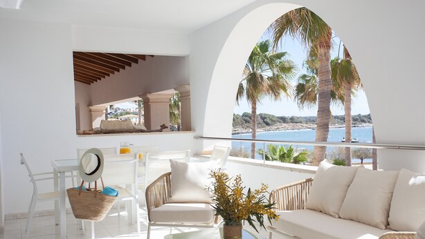 A modern room with a balcony, white furniture, and a view of the sea.