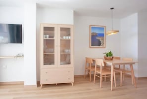 A dining area with a wooden table and chairs, a cabinet with glass doors, a hanging pendant light, and a framed picture on the wall. - Apartment 'Edificio Puerto - 3 Habitaciones G1' (Colonia Sant Jordi)