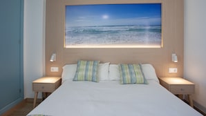 A bedroom with a large bed, two bedside tables, a nightstand, and a wall-mounted picture of a beach scene.
