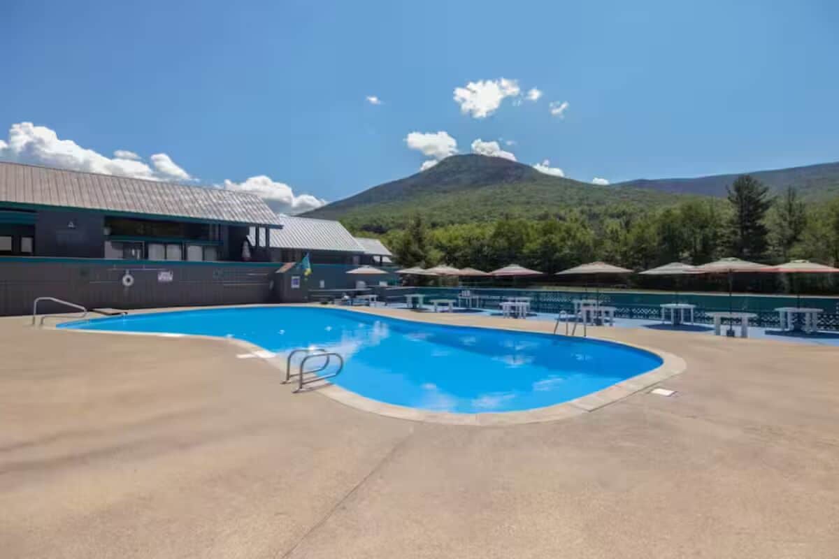 A pool area with a view of a mountain, tables, and umbrellas.