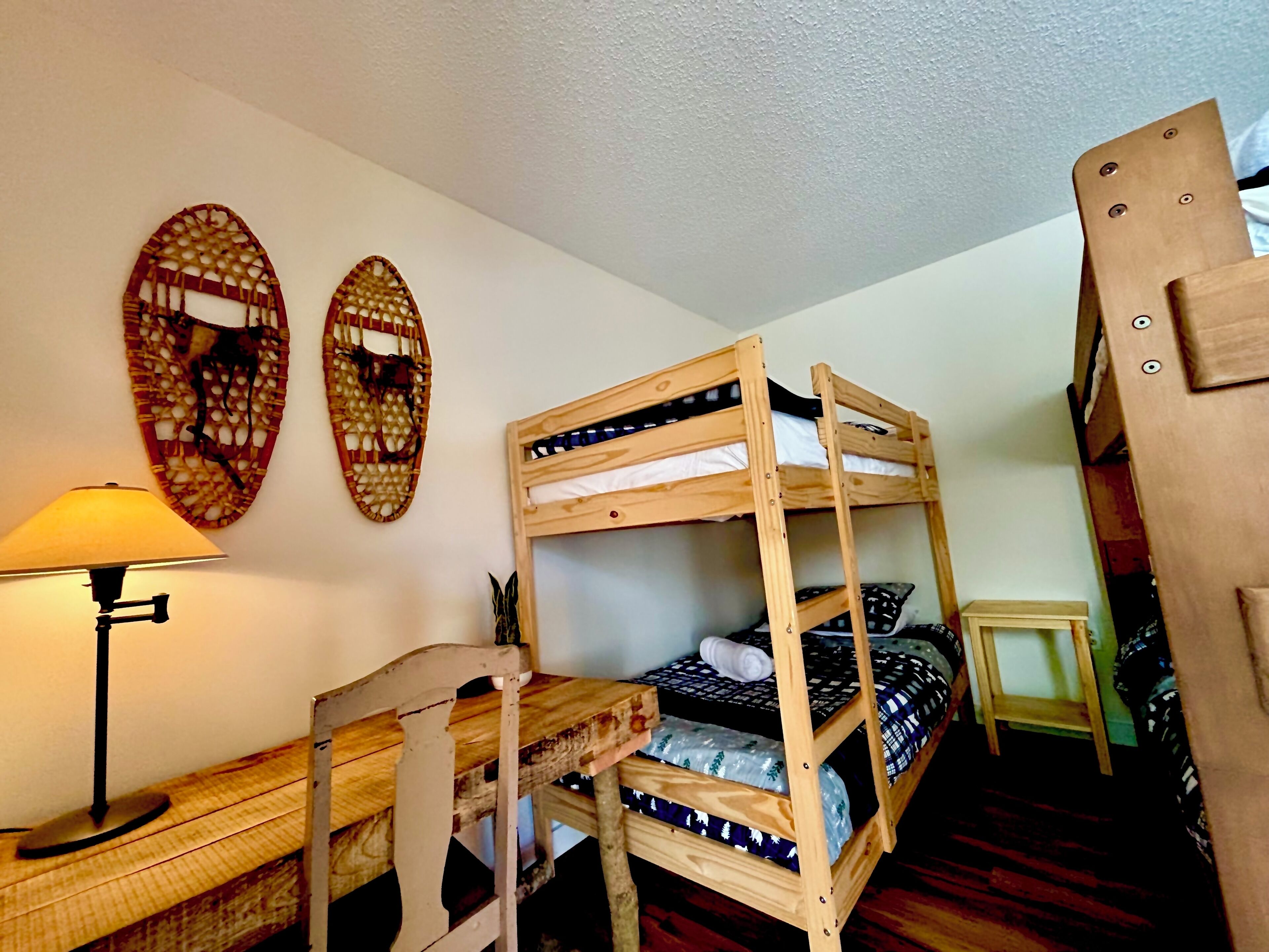 A bunk bed with a wooden frame, a small table with a lamp, and two wall decorations.