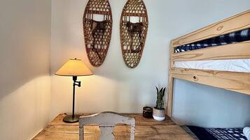 Een kleine kamer met een houten bureau, een stoel, een lamp, een stapelbed en twee decoratieve wandpanelen.