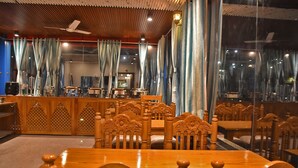 A restaurant with wooden furniture, a counter, and large windows with curtains. - Hotel US Tower (Devaprayāg)