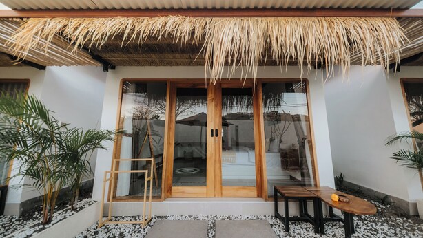 A modern building with a thatched roof entrance, wooden doors, and a small outdoor seating area with a table and chairs. - Hiraya Uluwatu (Pecatu)