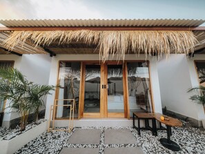 A modern building with a thatched roof entrance, wooden doors, and a small outdoor seating area with a table and chairs. - Hiraya Uluwatu (Pecatu)