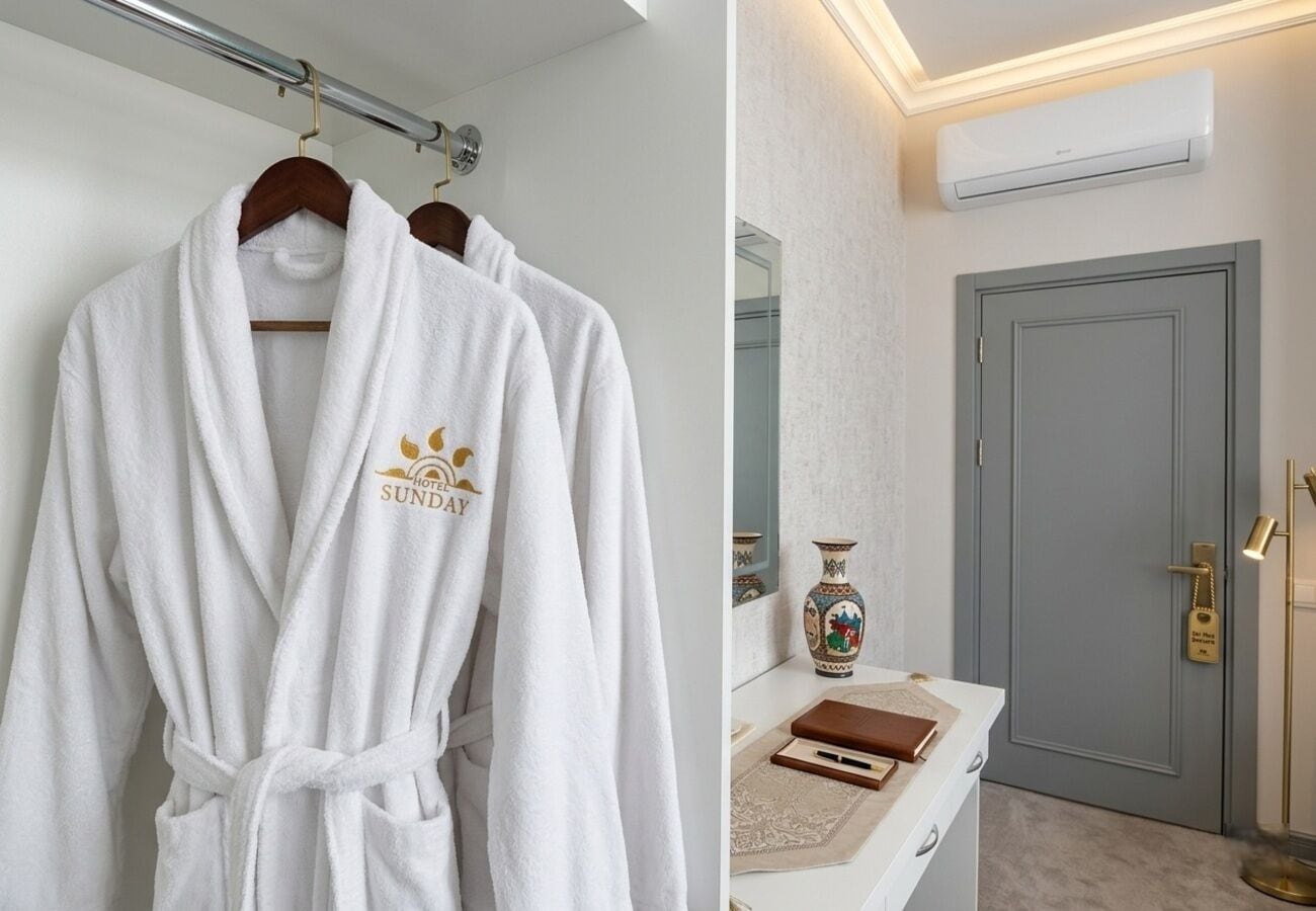 A white robe with a logo hanging on a rack, a bathroom vanity with a vase, and a door with a lock.