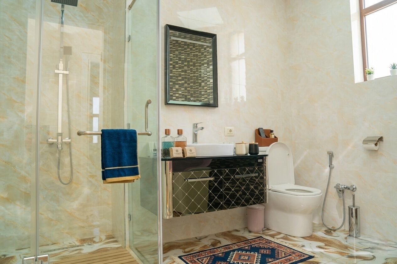 Ein Badezimmer mit Duschkabine aus Glas, Toilette, Waschbecken mit Spiegel darüber und einem gemusterten Teppich.