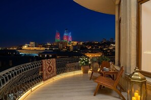 A balcony with a view of two illuminated buildings, a table with chairs, and a decorative lantern. - Sunday Hotel (Baku)