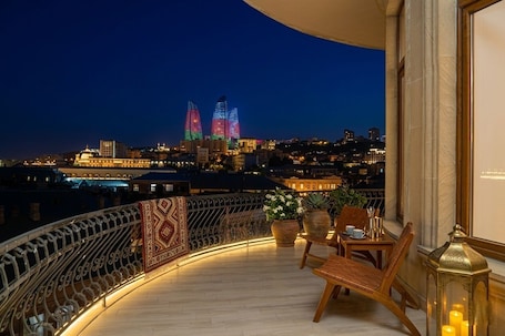 A balcony with a view of two illuminated buildings, a table with chairs, and a decorative lantern.