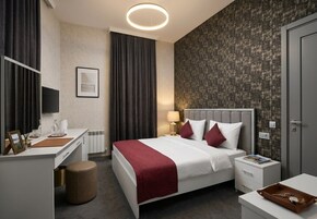 Een hotelkamer met een bed, nachtkastje, lamp en bureau met stoel.