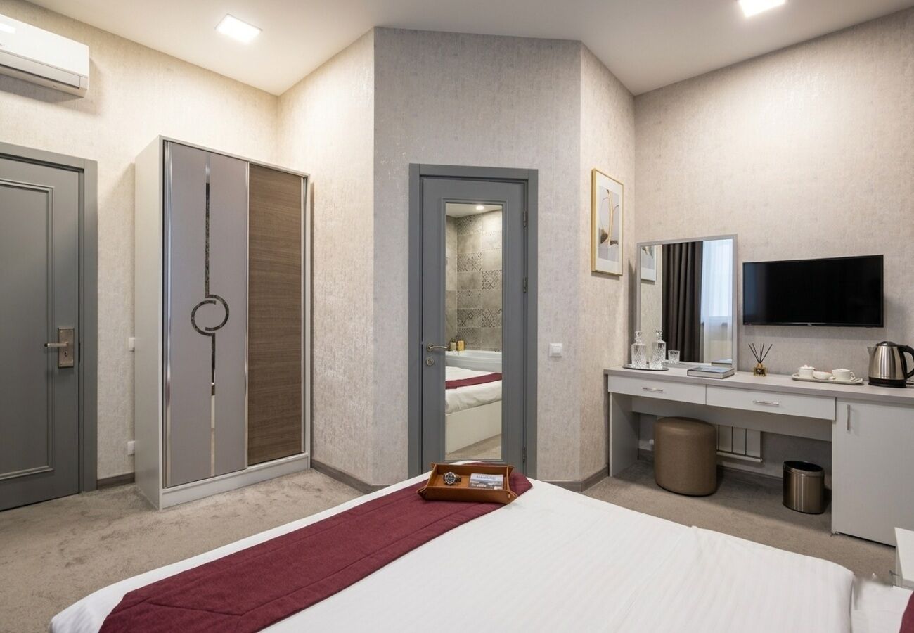 Habitación de hotel con cama, escritorio, televisión, armario y baño visible a través de una puerta abierta.