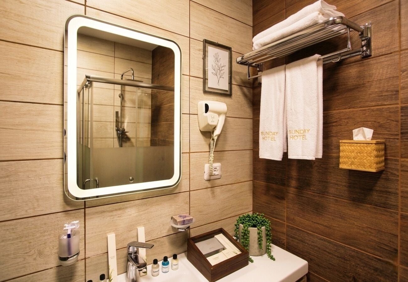 A bathroom with a wooden wall, a mirror, a towel rack, a hand dryer, and a small plant.