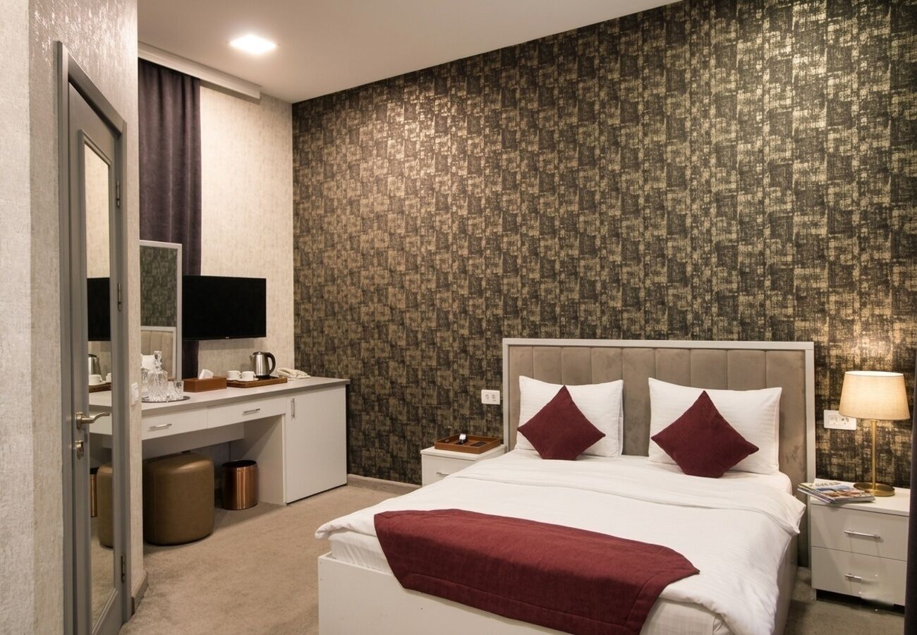 A hotel room with a bed, bedside tables, a desk, and a mirror.