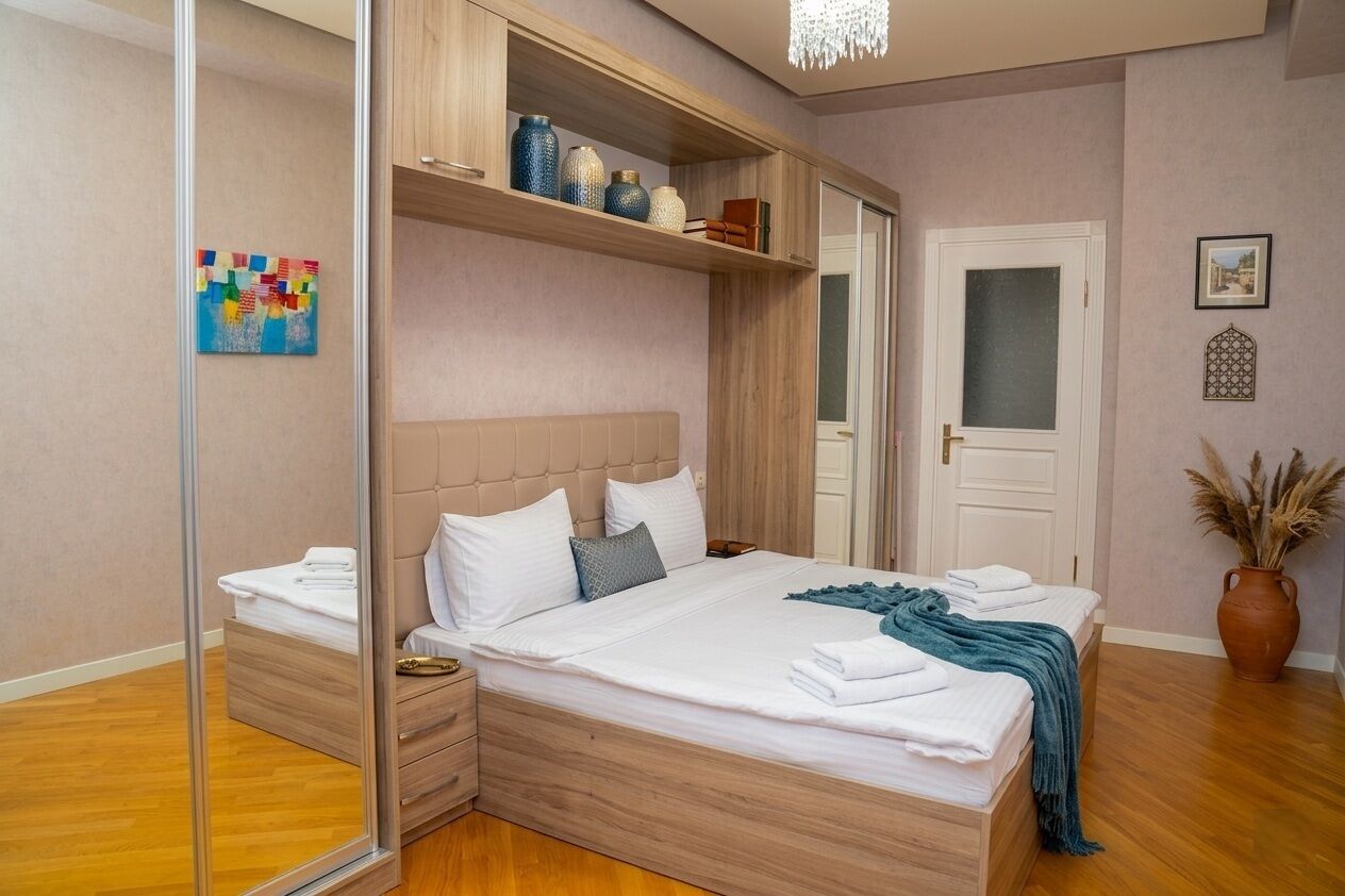 A bedroom with a bed, bedside tables, a mirror, a wardrobe, and a decorative vase.