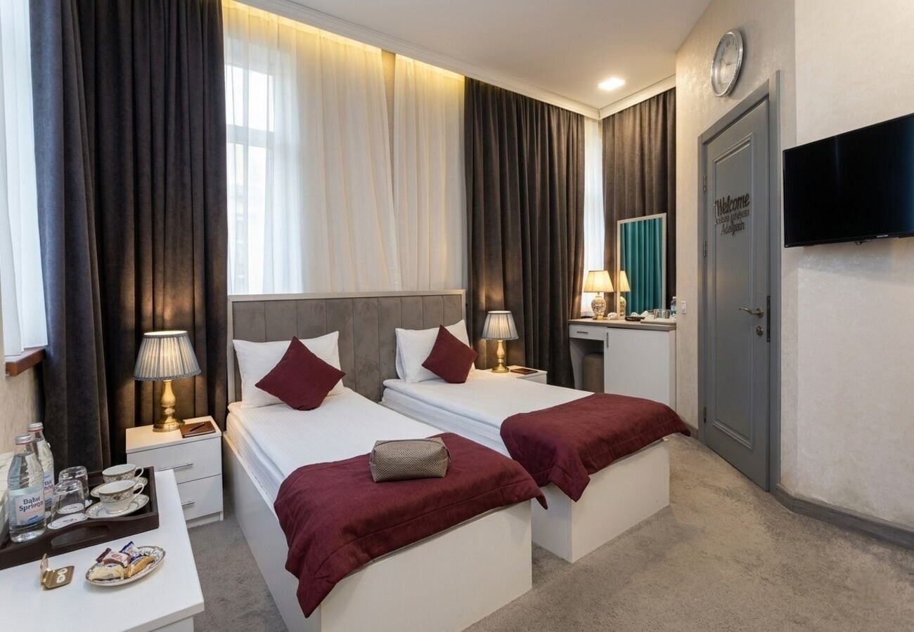 Hotelkamer met twee bedden, een televisie, een bureau met lamp, een klok en een deur met een welkomstbord.