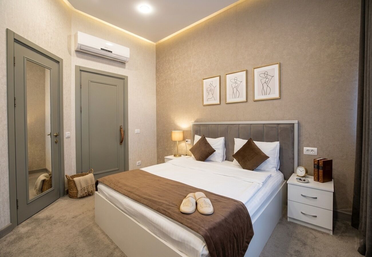 A hotel room with a bed, bedside tables, a nightstand, a mirror, and artwork on the wall.