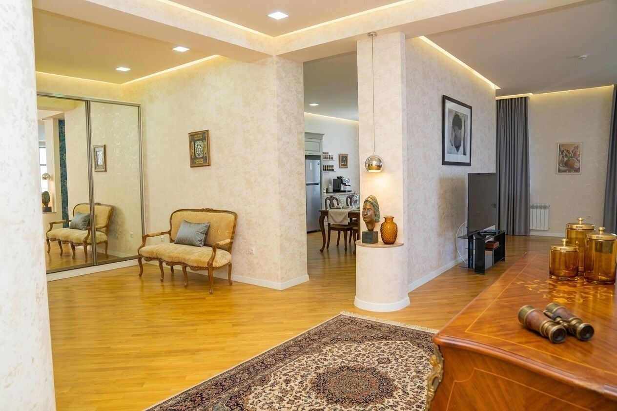 Een ruime woonkamer met een grote spiegel, een bank, een salontafel en een vloerkleed.