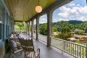 A covered outdoor deck with seating, a view of a forested area, and a distant town. - Marshall Inn Grand Porch Guestroom, Walk Downtown (Marshall)