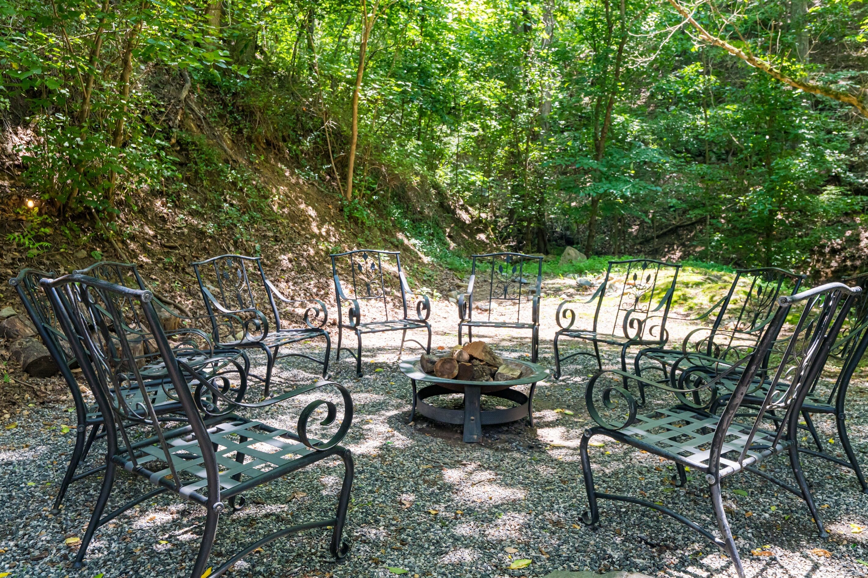 A circular outdoor seating area with metal chairs and a central fire pit surrounded by gravel.