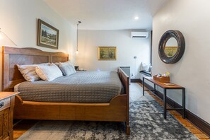 Un dormitorio ordenado con una cama de madera, una mesita de noche, un banco y un espejo en la pared.