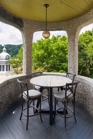 Un espacio de estar al aire libre cubierto con una mesa redonda y cuatro sillas, rodeado de pilares de piedra, con vistas a un paisaje verde exuberante y un edificio lejano con una cúpula.
