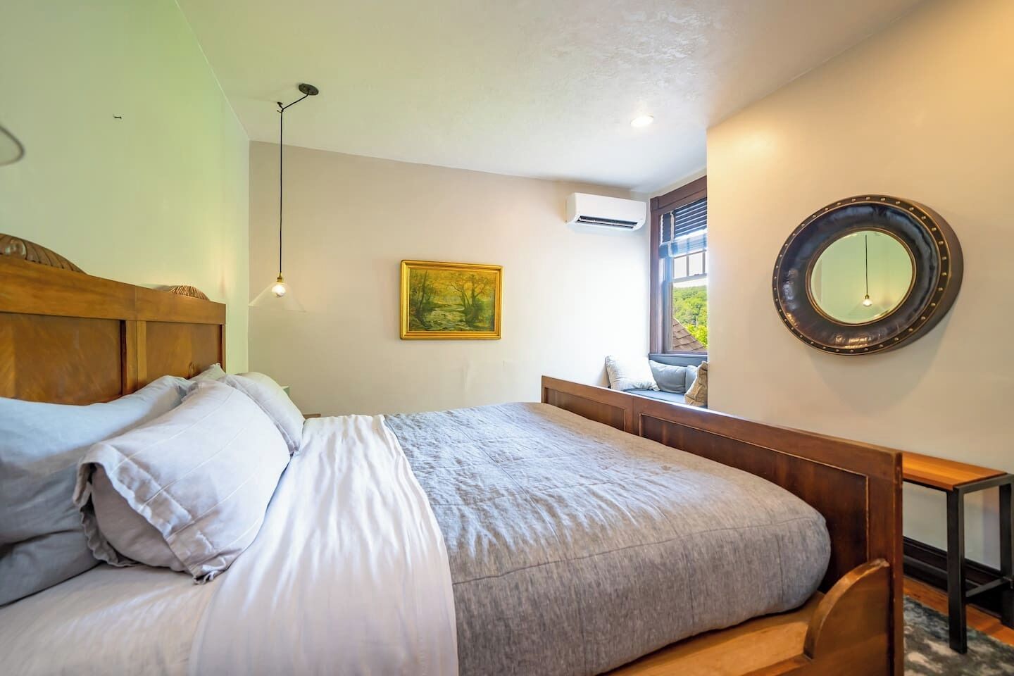 A bedroom with a wooden bed, a bedside table, a mirror, and a window with a view.