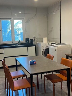 A modern kitchen with a dining area, including a table and chairs, a washing machine, and a coffee maker.
