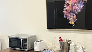 Een kitchenette met een magnetron, broodrooster en koffiezetapparaat op een houten tafel.