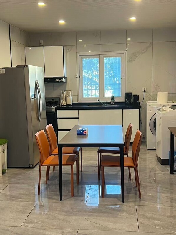 A modern kitchen with a central island, a refrigerator, a washing machine, and a dining area with chairs.