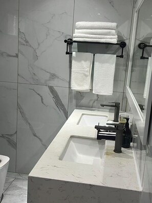 A modern bathroom with a marble sink, a glass shower enclosure, and a towel rack with folded towels.