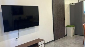 Moderni olohuone, jossa on suuri, seinälle asennettu taulutelevisio, puinen TV-taso laatikoineen, ovi ja jääkaappi.