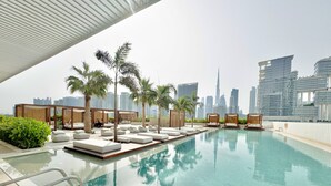 A rooftop infinity pool with lounge chairs and palm trees, overlooking a city skyline with modern buildings. - Modern Studio Burj Khalifa View Upside Living (Dubai)