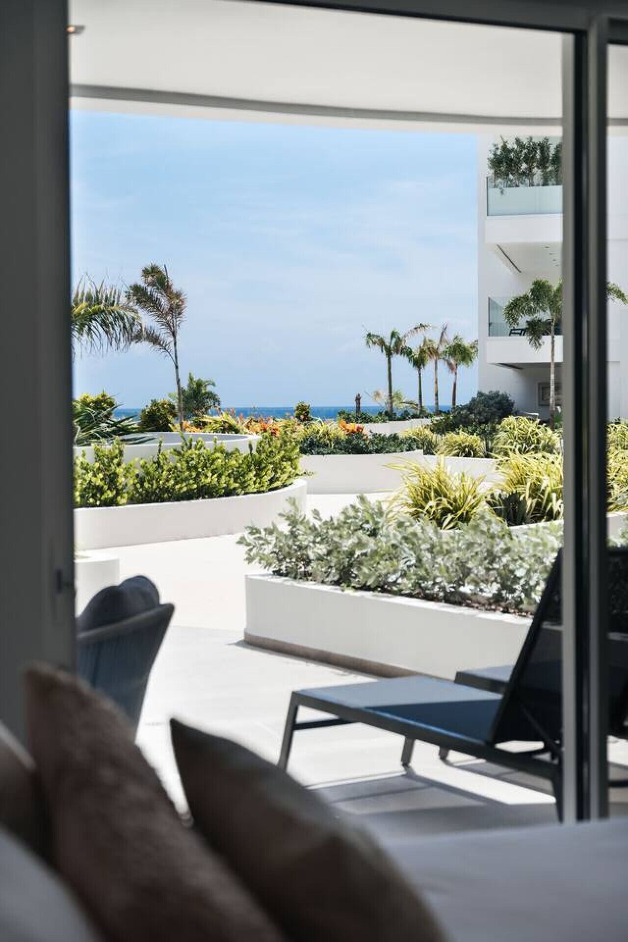 Ein modernes Hotelzimmer mit Balkon und Blick auf einen angelegten Garten sowie den Ozean.