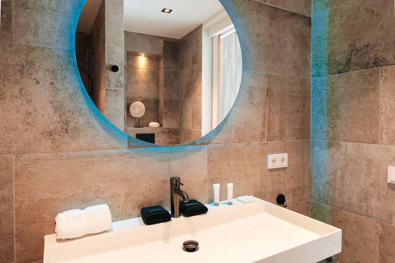 A bathroom with a large round mirror, a white sink, and a towel rack.