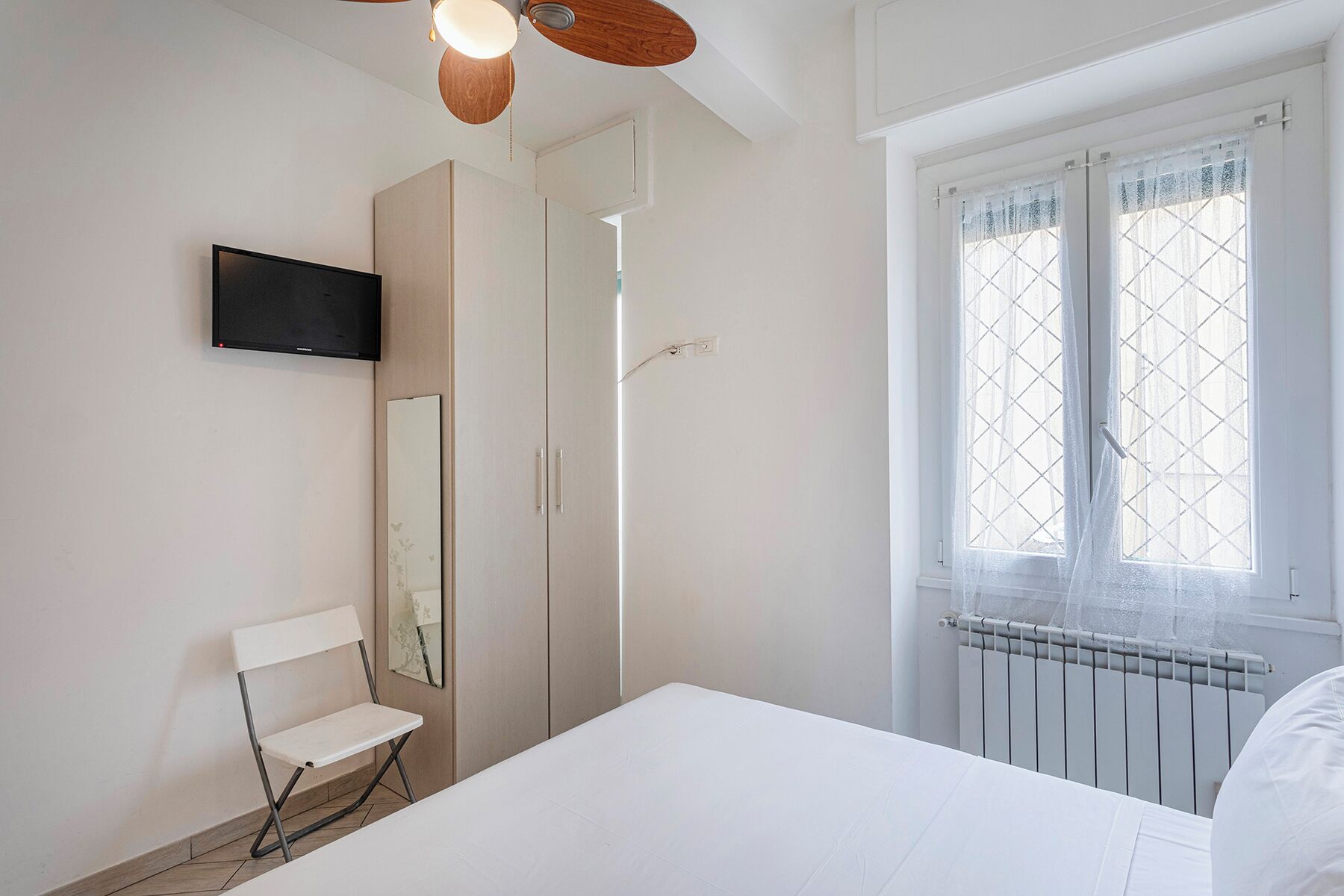A bedroom with a bed, a TV, a wardrobe, and a window with a view of the outside.