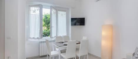 Een moderne eethoek met een tafel, stoelen, een aan de muur bevestigde televisie en een staande lamp.