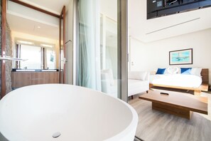 A modern bathroom with a large white bathtub, a wooden vanity, and a glass shower enclosure. - Sea Theatre Kata by ROI (Karon)