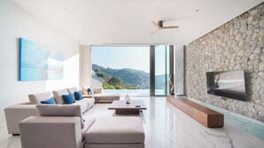 Ein modernes Wohnzimmer mit großem Fenster, einem an einer Steinwand montierten Flachbildfernseher und einem Deckenventilator.