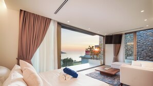 Ein modernes Hotelzimmer mit einem großen Bett, einer Couch und Blick auf den Sonnenuntergang über dem Meer.