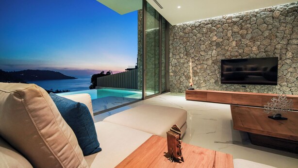 Ein modernes Wohnzimmer mit Steinwand, Flachbildfernseher und Meerblick.