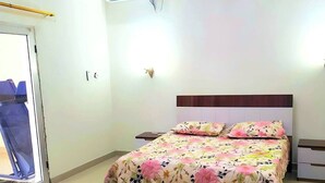 Une chambre à coucher comprenant un lit, une chaise, un bureau, un appareil de climatisation et un luminaire fixé au mur.