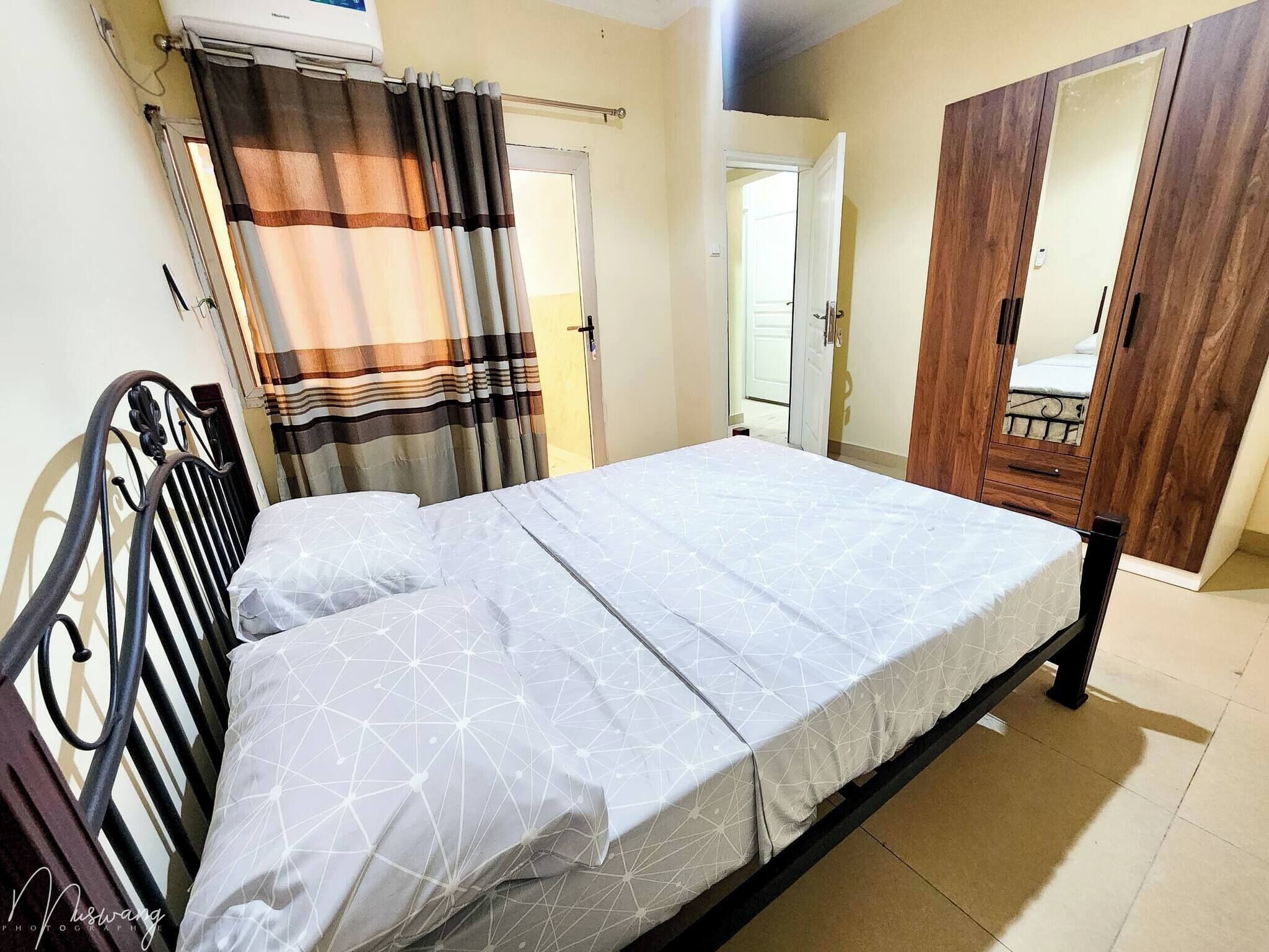 A bedroom with a bed, curtains, a wardrobe, and a door.