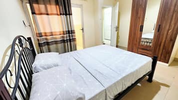 A bedroom with a bed, curtains, a wardrobe, and a door.