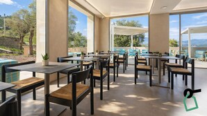 A spacious outdoor dining area with multiple tables and chairs, large windows offering scenic views, and a stone wall in the background. - Hotiday Lerici Trebiano (Arcola)
